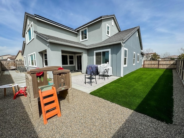 back of house with board and batten siding, a patio, a yard, and a fenced backyard