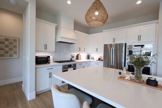 kitchen featuring white cabinetry, custom range hood, appliances with stainless steel finishes, light countertops, and a kitchen bar