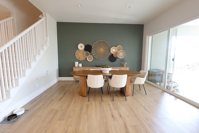 dining area with baseboards, an accent wall, light wood-style floors, and stairway