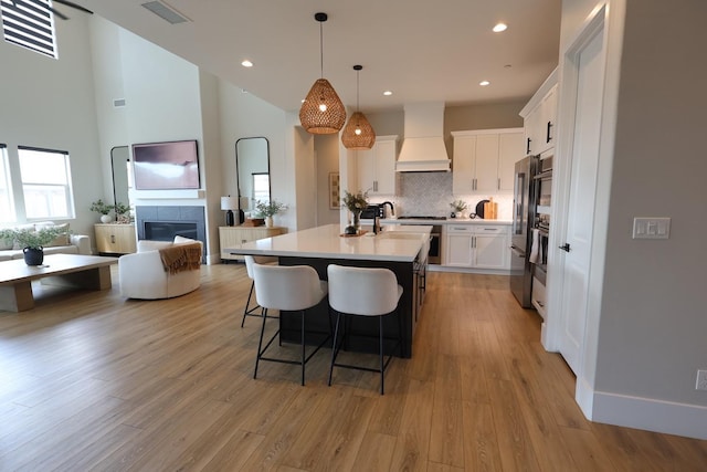 kitchen featuring a kitchen island with sink, custom exhaust hood, a tile fireplace, a kitchen bar, and visible vents