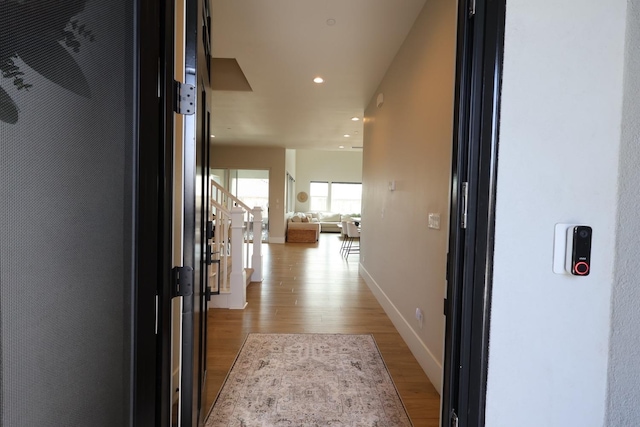 corridor with light wood finished floors, recessed lighting, stairway, and baseboards