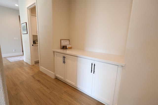 hall featuring baseboards, light wood-type flooring, and recessed lighting