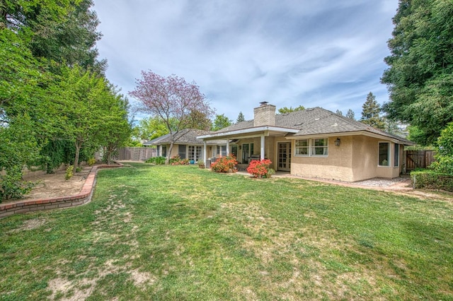 back of property with a fenced backyard, a chimney, a yard, and stucco siding