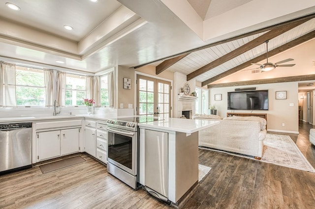 kitchen with a sink, appliances with stainless steel finishes, a fireplace, and lofted ceiling with beams