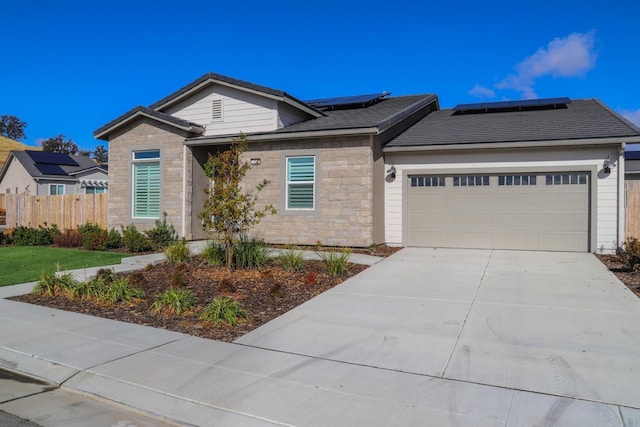 single story home with driveway, solar panels, a garage, fence, and stone siding