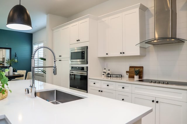 kitchen featuring wall chimney range hood, white cabinets, stainless steel appliances, and a sink