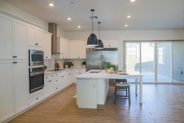 kitchen featuring a kitchen island with sink, visible vents, light wood-style floors, built in appliances, and wall chimney exhaust hood