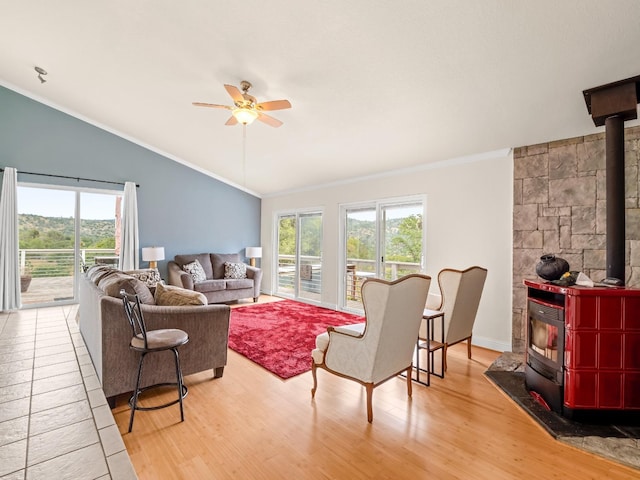 living room featuring ceiling fan, vaulted ceiling, a wood stove, ornamental molding, and light wood-style flooring