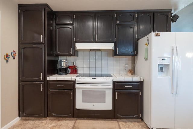 kitchen with tile countertops, backsplash, under cabinet range hood, and white appliances