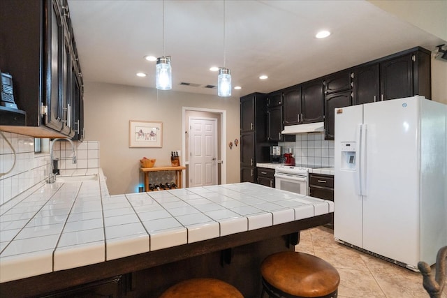 kitchen with a sink, white appliances, tile counters, a peninsula, and under cabinet range hood