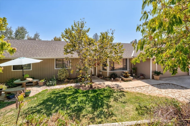 view of front facade featuring concrete driveway, an attached garage, a shingled roof, and a front lawn