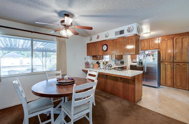 827 N Armstrong Ave, Clovis, CA 93611 - kitchen with appliances with stainless steel finishes, brown cabinetry, a peninsula, tile counters, and a textured ceiling