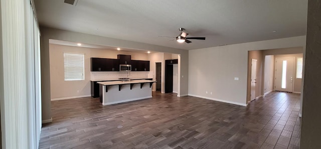 kitchen featuring ceiling fan, a kitchen island with sink, stainless steel microwave, open floor plan, and dark wood-type flooring