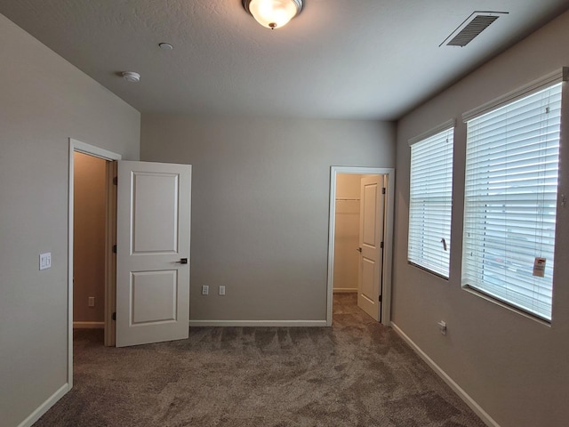 unfurnished bedroom featuring visible vents, baseboards, carpet floors, and a spacious closet