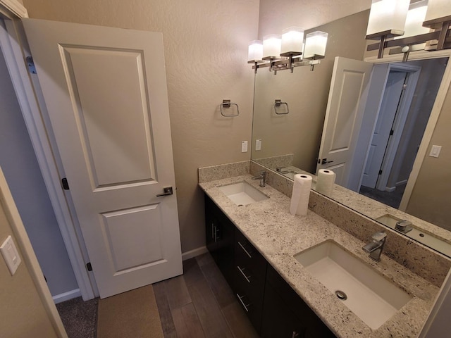 full bathroom with a sink, baseboards, double vanity, and wood finished floors