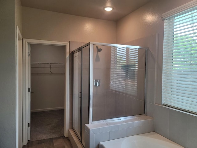 bathroom featuring a shower stall, a walk in closet, a bath, and wood finished floors