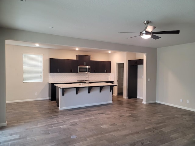 kitchen featuring a breakfast bar, a sink, an island with sink, a ceiling fan, and stainless steel microwave
