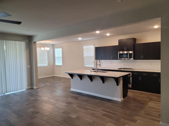 kitchen featuring gas cooktop, an inviting chandelier, a sink, stainless steel microwave, and a kitchen bar