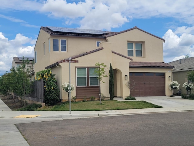 mediterranean / spanish home with fence, a tile roof, a garage, concrete driveway, and solar panels