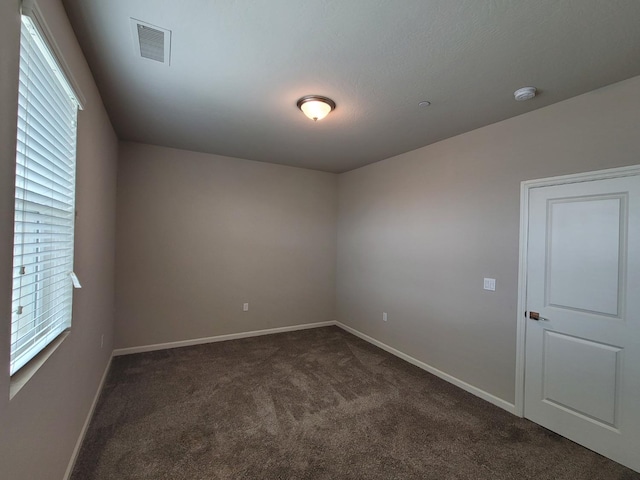 spare room with dark carpet, baseboards, and visible vents