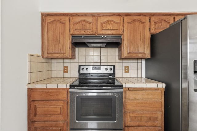 4462 N Manila Ave, Fresno, CA 93727 - kitchen with stainless steel appliances, under cabinet range hood, tile counters, decorative backsplash, and brown cabinets