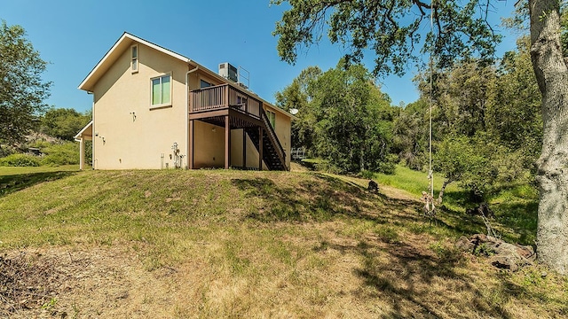 back of house with stairs, stucco siding, a deck, a chimney, and a yard