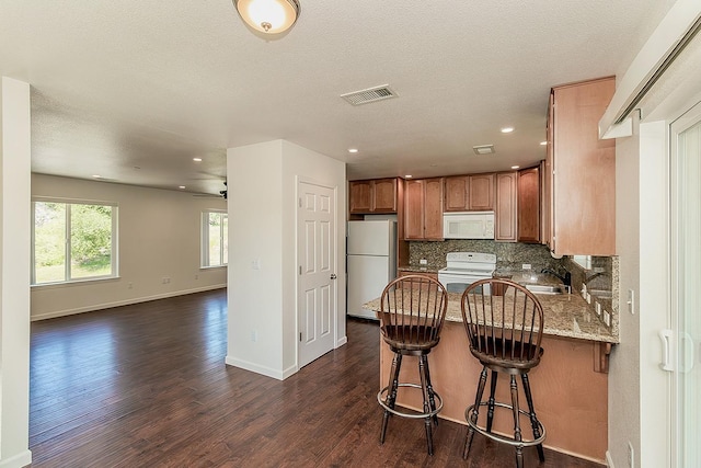 kitchen featuring white appliances, dark wood finished floors, brown cabinetry, a peninsula, and backsplash