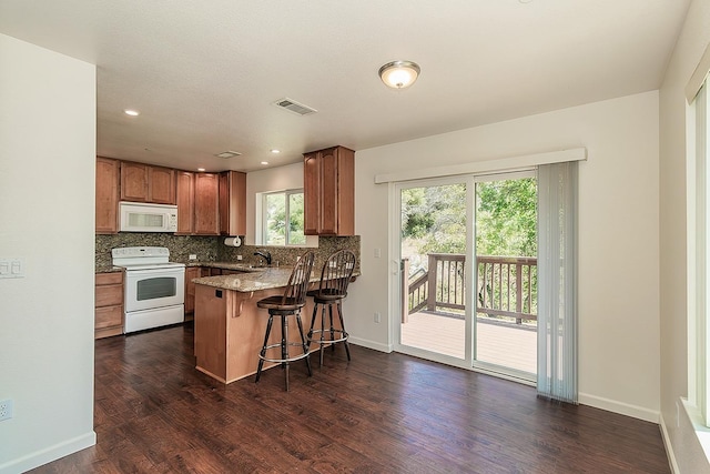 kitchen featuring visible vents, a peninsula, white appliances, a kitchen bar, and dark wood finished floors
