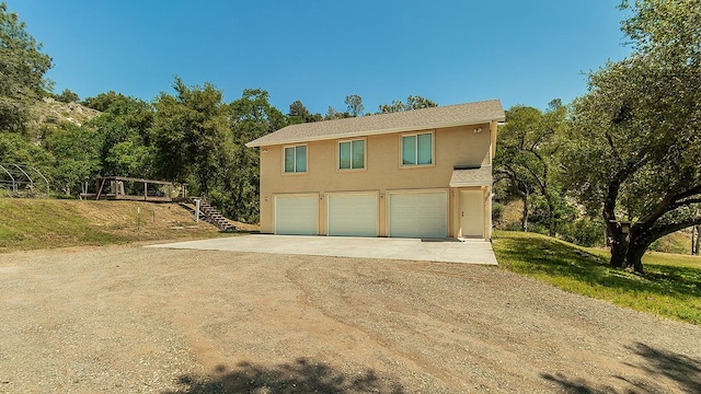 view of front of home with an attached garage, dirt driveway, stucco siding, and stairs
