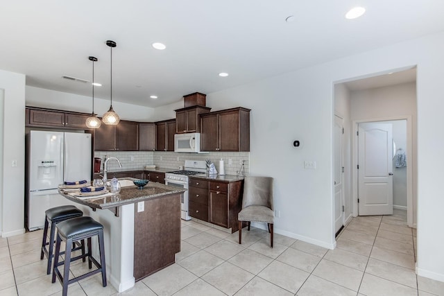 kitchen with light tile patterned flooring, dark brown cabinetry, white appliances, dark stone counters, and visible vents