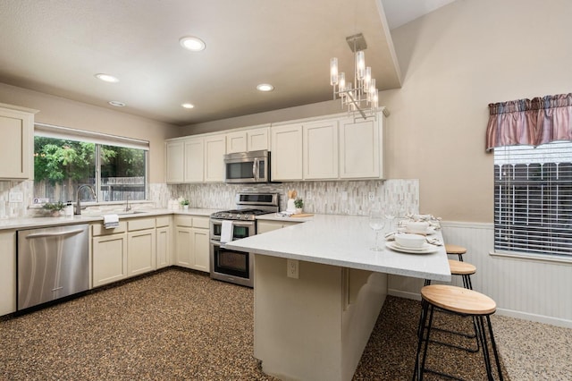 4650 W Chennault Ave, Fresno, CA 93722 - kitchen featuring stainless steel appliances, a wainscoted wall, a peninsula, light countertops, and a kitchen breakfast bar