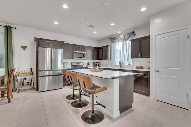 kitchen with dark brown cabinetry, a kitchen island, a kitchen bar, light countertops, and appliances with stainless steel finishes