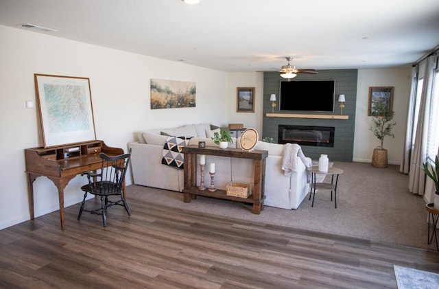 living room with ceiling fan, visible vents, a large fireplace, and wood finished floors