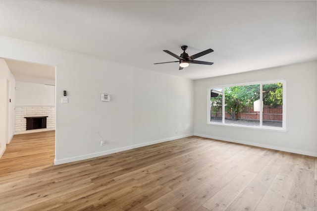 empty room with light wood-type flooring, a ceiling fan, baseboards, and a brick fireplace