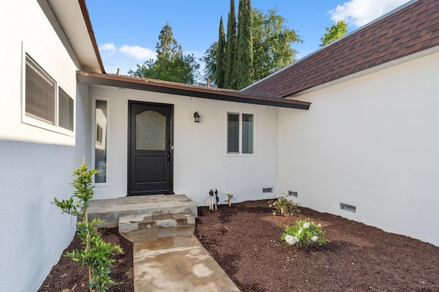 property entrance with a shingled roof, stucco siding, and crawl space