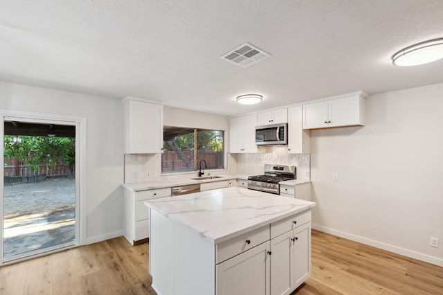 kitchen with visible vents, a sink, light wood finished floors, backsplash, and stainless steel appliances