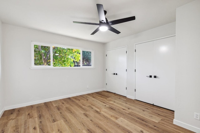 unfurnished bedroom with two closets, baseboards, and wood finished floors
