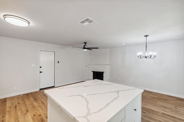 unfurnished living room with visible vents, light wood-style flooring, ceiling fan with notable chandelier, and baseboards