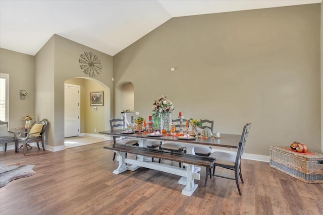 dining space featuring baseboards, arched walkways, wood finished floors, and high vaulted ceiling