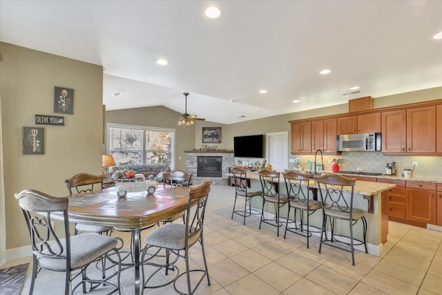 dining room with a glass covered fireplace, vaulted ceiling, a ceiling fan, and light tile patterned flooring