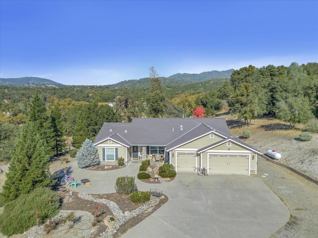 ranch-style home featuring concrete driveway, an attached garage, a mountain view, and a view of trees