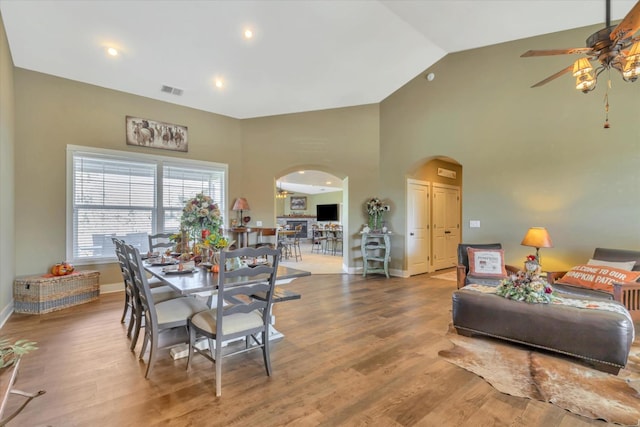 dining area featuring ceiling fan, arched walkways, wood finished floors, baseboards, and high vaulted ceiling