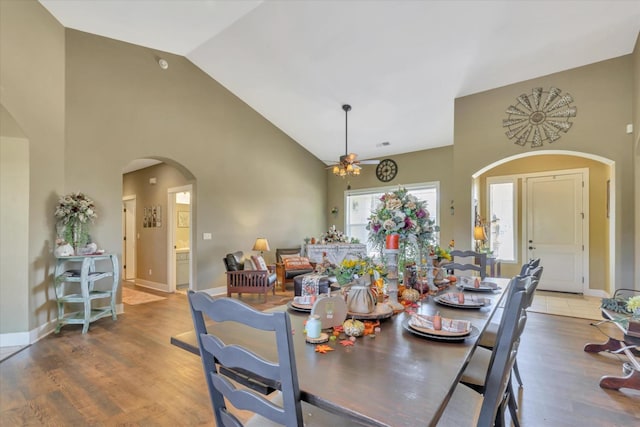 dining area featuring arched walkways, high vaulted ceiling, a ceiling fan, baseboards, and wood finished floors