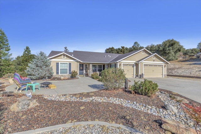 single story home with concrete driveway, an attached garage, a fire pit, and stone siding