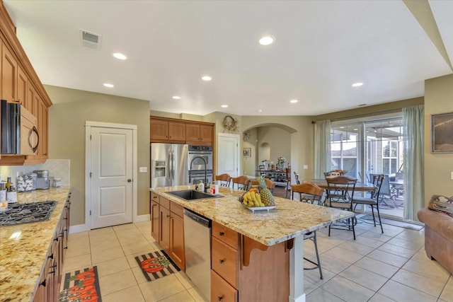 kitchen with appliances with stainless steel finishes, a sink, arched walkways, a kitchen breakfast bar, and light tile patterned floors