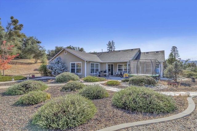 single story home featuring a patio, a trampoline, and roof with shingles