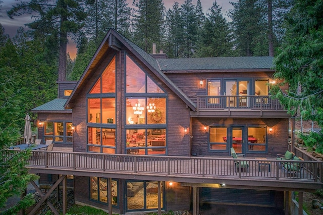 40596 Wild Iris Ln, Shaver Lake, CA 93664 - back of house at dusk with a garage, a wooden deck, a shingled roof, and a balcony