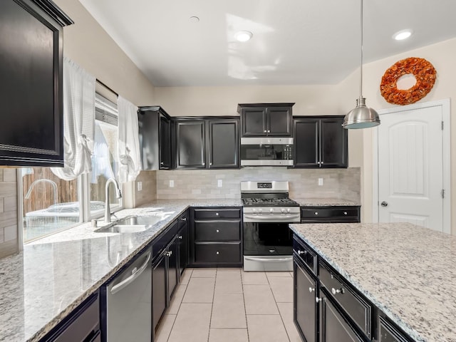 kitchen with hanging light fixtures, a sink, dark cabinets, stainless steel appliances, and backsplash