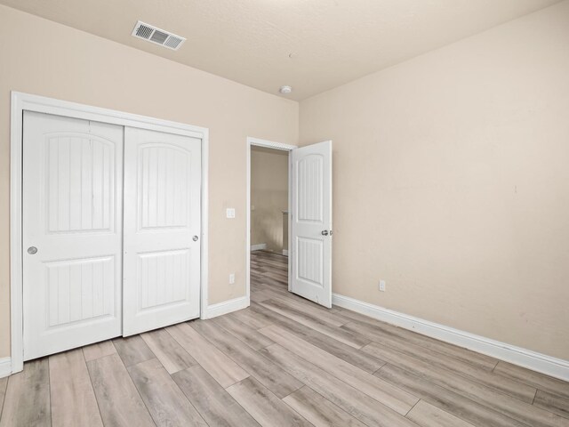 unfurnished bedroom with baseboards, a closet, light wood-style flooring, and visible vents