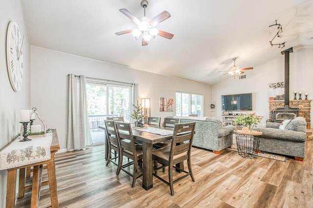 dining area featuring ceiling fan, lofted ceiling, light wood-style flooring, and a wood stove